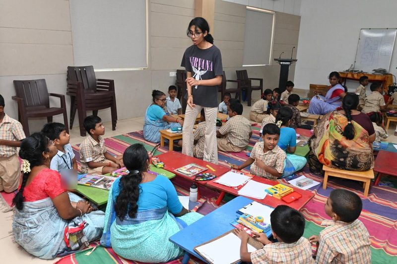 Shruti Arvind standing among children and teachers seated on mats during an art workshop